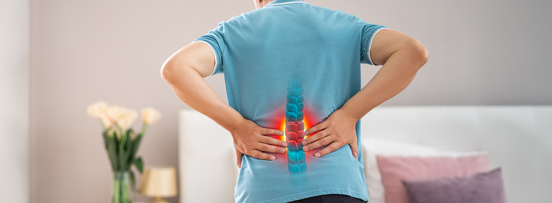 This is an image of a person standing with their back towards the camera, appearing to have a red area on their back, possibly indicating pain or discomfort, against a blurred background that suggests an indoor living space.