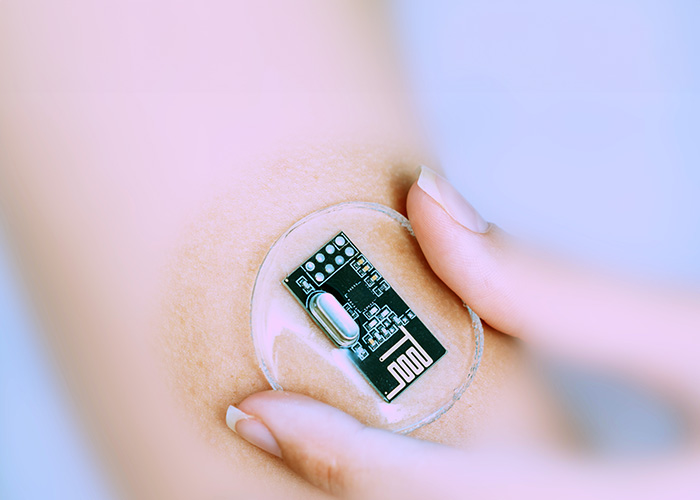 A person s hand holding a small electronic device with a clear circular top over a bandage on their arm.