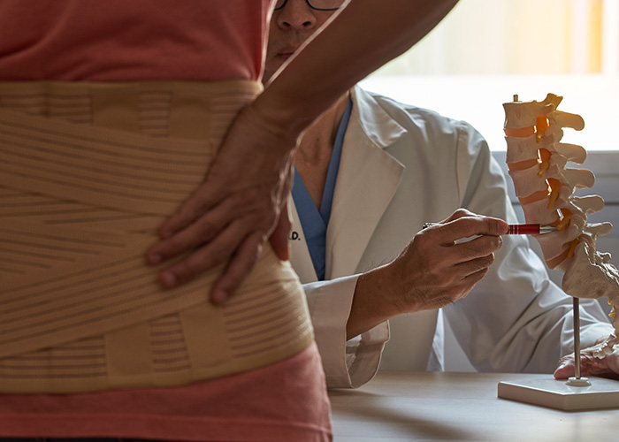 The image shows a person receiving spinal care from a practitioner, with a medical model illustrating the spine and spinal column.